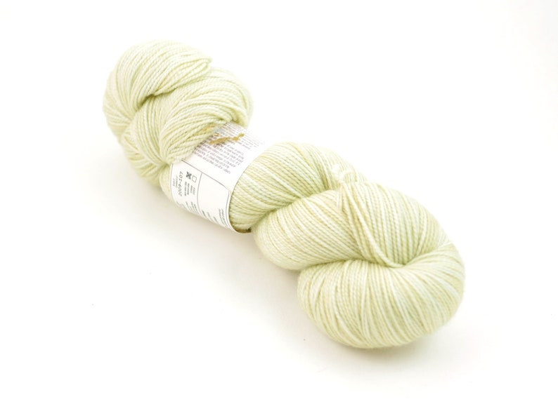 May include: A skein of pale green yarn, with a white label that reads "The Loopy Ewe - Superwash Merino - 100g - 420 yards - 100% Superwash Merino Wool - Hand Dyed in the USA - Machine Washable - Made in the USA".