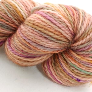 Peut inclure: Une pelote de laine multicolore aux tons pêche, rose, beige et vert. La laine est bien torsadée, révélant la texture des fibres. Les couleurs se fondent, créant un effet nuancé. Idéale pour les projets de tricot ou de crochet.