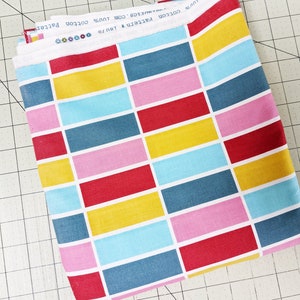 May include: A folded piece of fabric with a geometric pattern of red, yellow, blue, and pink rectangles. The fabric is labelled "Pattern & Twillo 100% Cotton cottons.com".