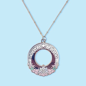 A gold tone necklace chain with an art nouveau style sailor moon gold and enamel pendant featuring the planetary symbols on the outside. The bottom has flowers and a silver crystal lotus with a gem. The middle has a cutout with a gold crescent moon.