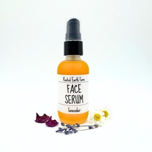 May include: A clear glass bottle with a black pump top filled with a yellow liquid. The bottle has a white label that reads "Rooted Earth Farm Face Serum lavender".