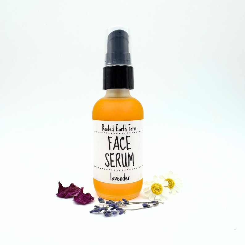 May include: A clear glass bottle with a black pump top filled with a yellow liquid. The bottle has a white label that reads "Rooted Earth Farm Face Serum lavender".
