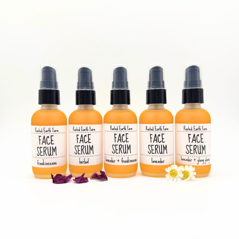 May include: Five amber glass bottles with black pump tops and white labels. The labels read "Rooted Earth Farm Face Serum" with different scents listed below: frankincense, herbal, lavender + frankincense, lavender, and lavender + ylang ylang.