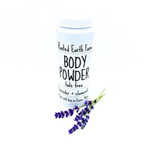 May include: White plastic jar with a black label that reads "Rooted Earth Farm BODY POWDER talc free lavender + chamomile Made with love in Casco, Maine". A sprig of lavender is next to the jar.