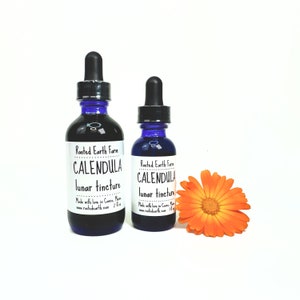 May include: Two blue glass bottles with droppers, labeled "Rooted Earth Farm Calendula Lunar Tincture". The bottles are next to a bright orange calendula flower.