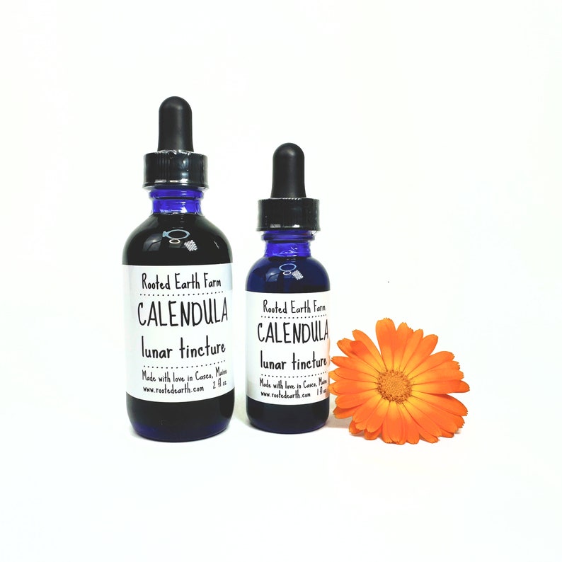 May include: Two blue glass bottles with droppers, labeled "Rooted Earth Farm Calendula Lunar Tincture". The bottles are next to a bright orange calendula flower.