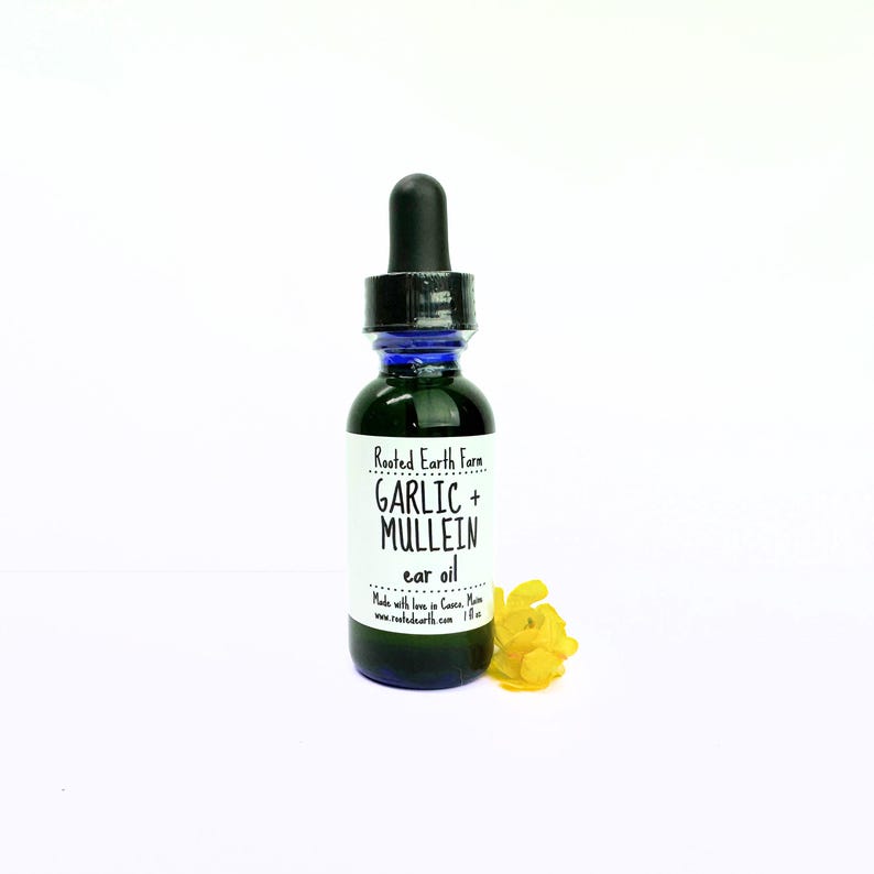 Puede incluir: Un peque&ntilde;o frasco de vidrio azul con un gotero. El frasco est&aacute; etiquetado con "Rooted Earth Farm Garlic + Mullein ear oil". El frasco est&aacute; sobre una superficie blanca con una flor amarilla.