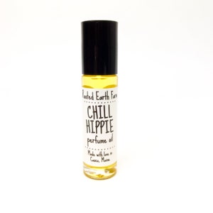 Puede incluir: Un peque&ntilde;o frasco de vidrio amarillo de aceite de perfume con un tap&oacute;n de rodillo negro. La etiqueta dice "Rooted Earth Farm Chill Hippie perfume oil Made with love in Casco, Maine."