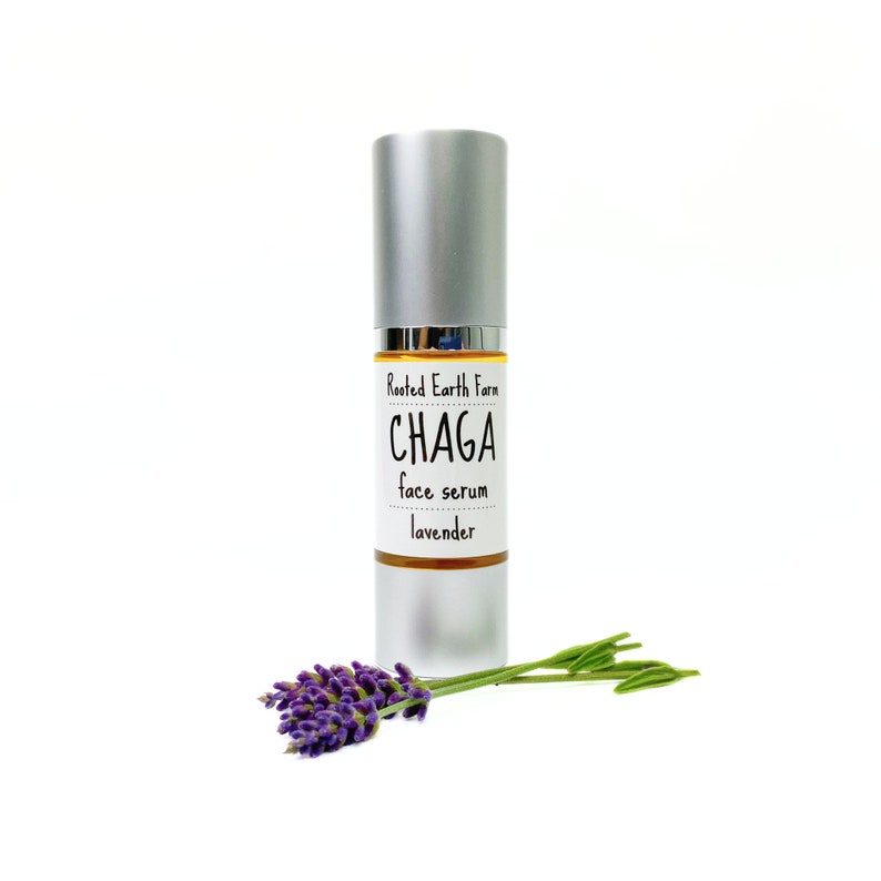 Pode incluir: Um frasco prateado com um r&oacute;tulo branco que diz "Rooted Earth Farm CHAGA face serum lavender". Um ramo de lavanda est&aacute; em primeiro plano.