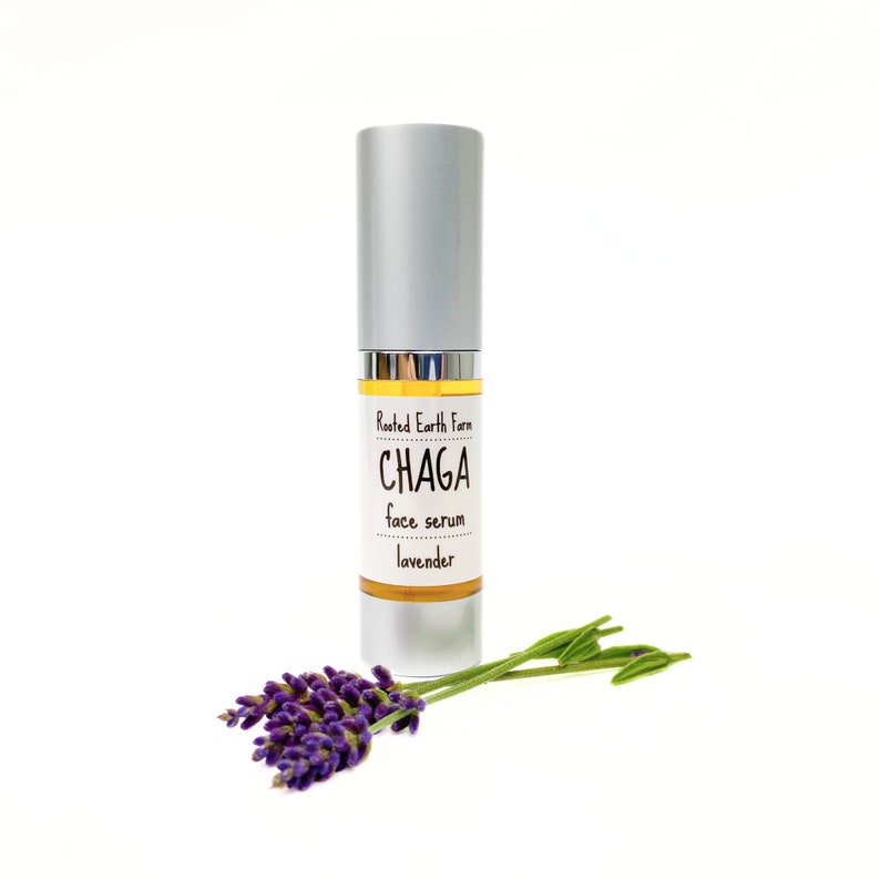 Pode incluir: Um frasco prateado com um r&oacute;tulo branco que diz "Rooted Earth Farm CHAGA face serum lavender". Um ramo de lavanda est&aacute; em primeiro plano.