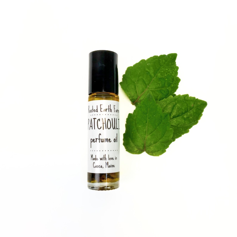 Op de afbeelding: Een klein glazen flesje Patchouli-parfumolie met een zwarte roll-on-dop. Het etiket vermeldt "Rooted Earth Farm Patchouli perfume oil Made with love in Casco, Maine".
