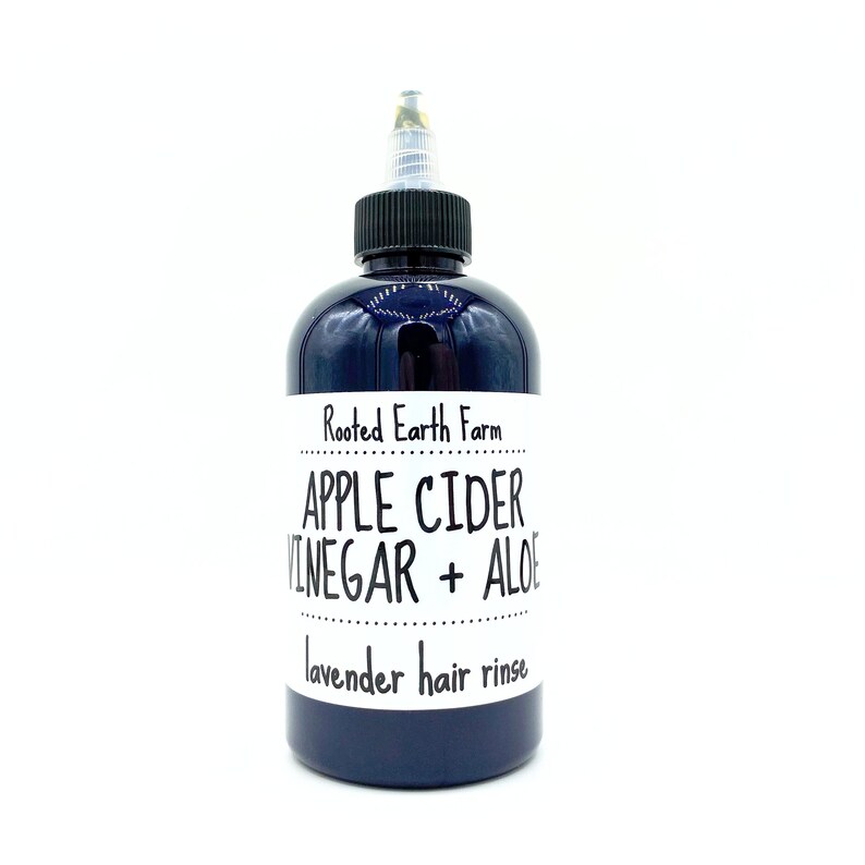 Op de afbeelding: Een donkerblauwe fles met een wit etiket waarop staat "Rooted Earth Farm Appelazijn + Alo&euml; Lavendel Haar Spoeling".