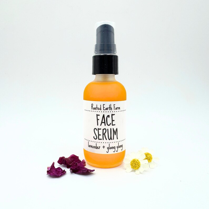 May include: A clear glass bottle with a black pump top filled with a yellow liquid. The bottle has a white label that reads "Rooted Earth Farm FACE SERUM lavender + ylang ylang".