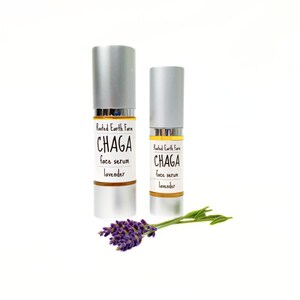 Pode incluir: Duas garrafas prateadas de Rooted Earth Farm Chaga face serum com lavanda. As garrafas est&atilde;o em um fundo branco com um ramo de lavanda.