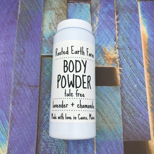 May include: White plastic jar of Rooted Earth Farm body powder, labeled "talc free lavender + chamomile" and "Made with love in Casco, Maine".