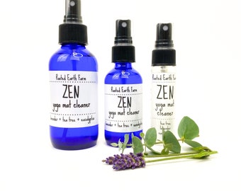 May include: Three blue glass bottles with spray tops labelled "Rooted Earth Farm ZEN yoga mat cleaner" with different scent combinations: lavender, tea tree, and eucalyptus. The bottles are arranged in a row from largest to smallest.