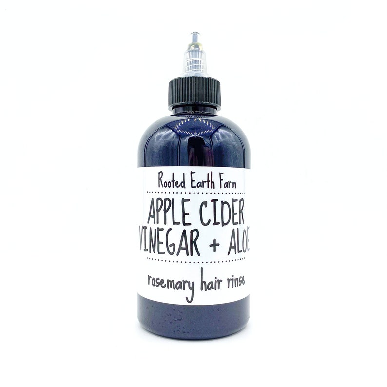 Op de afbeelding: Een donkerblauwe fles met een wit etiket waarop staat "Rooted Earth Farm Apple Cider Vinegar + Aloe rosemary hair rinse".