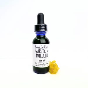 Puede incluir: Una peque&ntilde;a botella de vidrio verde oscuro con un gotero azul. La botella est&aacute; etiquetada "Rooted Earth Farm GARLIC + MULLEIN ear oil". Hecho con amor en Cave, MN. www.rootedearth.com