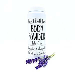 May include: White plastic jar with a black label that reads "Rooted Earth Farm BODY POWDER talc free lavender + chamomile Made with love in Casco, Maine". A sprig of lavender flowers is in front of the jar.