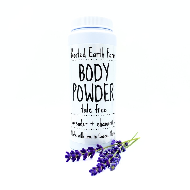 May include: White plastic jar with a black label that reads "Rooted Earth Farm BODY POWDER talc free lavender + chamomile Made with love in Casco, Maine". A sprig of lavender flowers is in front of the jar.