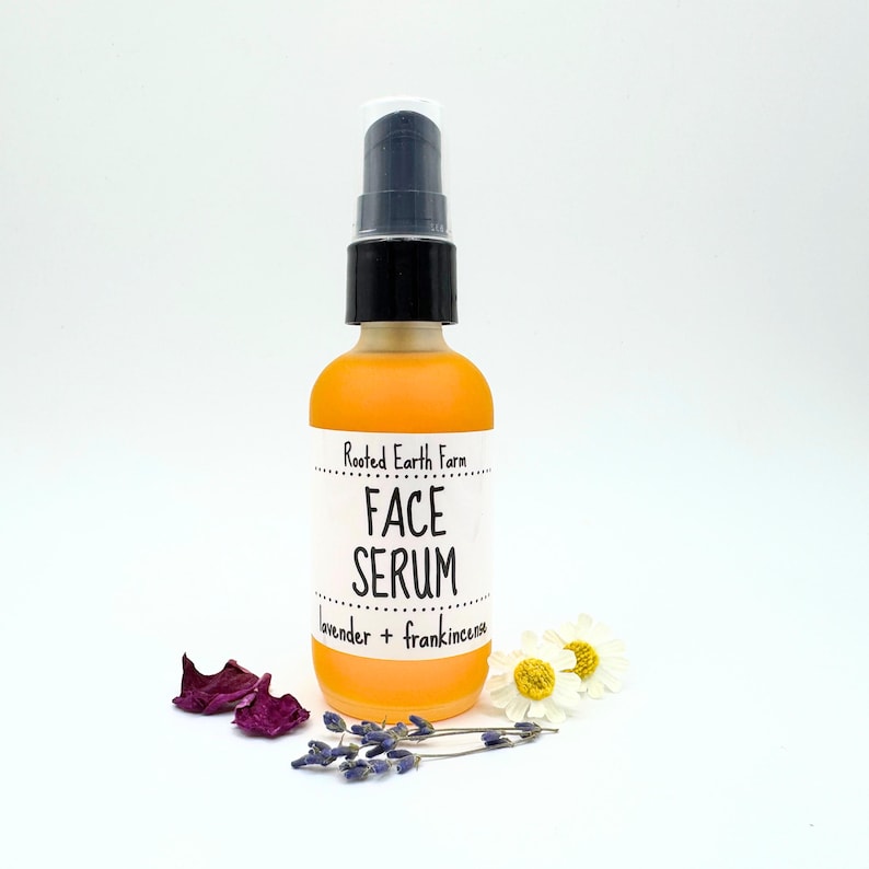 May include: A clear glass bottle with a black pump top filled with a yellow liquid. The bottle has a white label that reads "Rooted Earth Farm Face Serum Lavender + Frankincense".