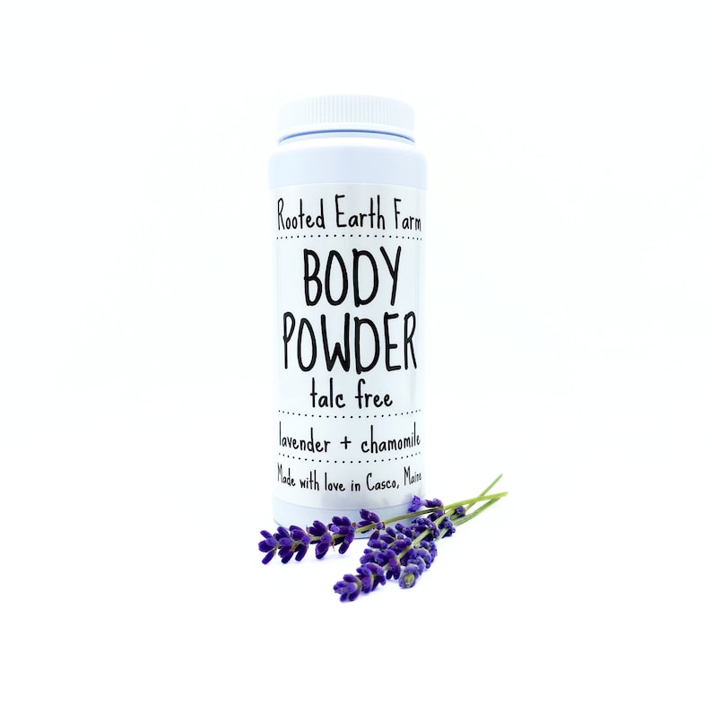 May include: White plastic jar with a black label that reads "Rooted Earth Farm BODY POWDER talc free lavender + chamomile Made with love in Casco, Maine".  A sprig of lavender flowers is in front of the jar.