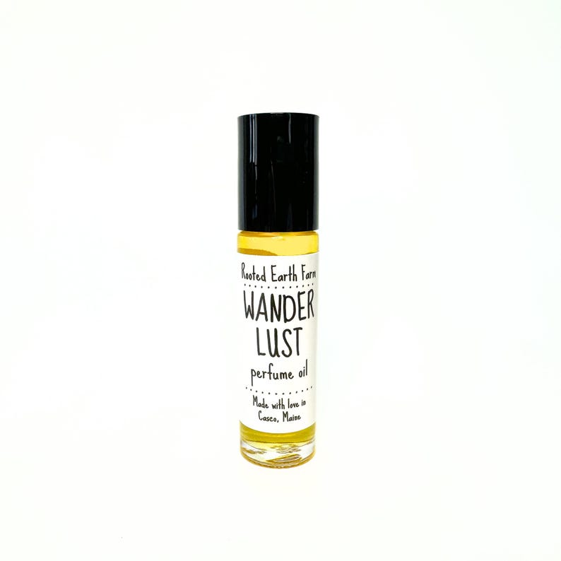 May include: A small glass bottle of perfume oil with a black roll-on top. The label reads "Rooted Earth Farm Wander Lust perfume oil Made with love in Casco, Maine."