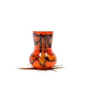 May include: A small, orange and brown ceramic vase with a unique abstract design. The vase has a rounded body and a narrow neck.