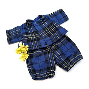 May include: A two-piece outfit consisting of a short-sleeved button-up shirt and matching trousers, both featuring a blue, black, and yellow plaid pattern. The trousers have elasticated cuffs at the bottom, and two small yellow flowers are attached.
