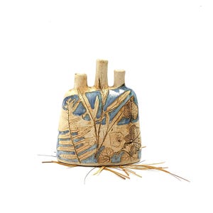 Peut inclure: Un vase en céramique à trois becs, beige et bleu. Le vase est orné de motifs de feuilles et de fougères. La base est décorée d'herbe séchée.