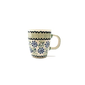 May include: A ceramic mug with a floral design. The mug features a light green rim with a black and white pattern, and a blue floral pattern on the body. The handle is light green.