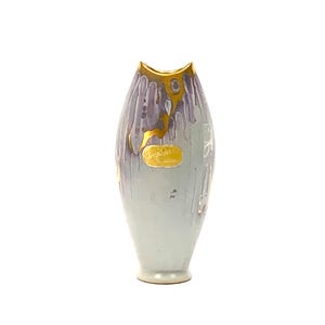 May include: A tall, tapered ceramic vase featuring a light blue and lavender drip glaze pattern. The rim and a central oval emblem are finished in metallic gold. The emblem displays embossed text that reads "Original" and "Keramik".