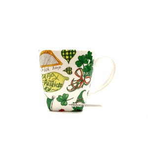 May include: White ceramic mug decorated with St. Patrick's Day illustrations. The design includes a golden harp, green shamrocks, a green leprechaun, and the text "Happy Patrick's Day". The mug has a curved handle.
