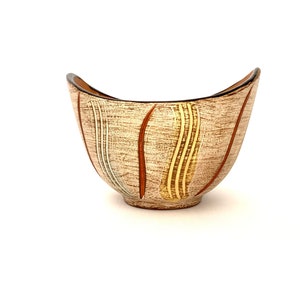 May include: A mid-century modern ceramic bowl with a textured beige surface. Vertical brown, yellow, and white stripes adorn the exterior. The rim is dark brown, and the bowl has a unique, curved shape.