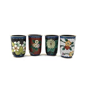 May include: Four decorative ceramic tumblers with floral designs. Each tumbler features a different pattern of flowers in various colors, set against a dark background. The rims are black, and the overall aesthetic is ornate.