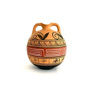 May include: A small, terracotta-coloured vase with two handles. The vase is decorated with black and red geometric patterns, including a key pattern and triangles. The base is black, and the design is reminiscent of ancient Greek pottery.