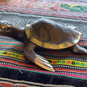 May include: A bronze turtle sculpture with a detailed shell and a textured finish. The turtle is lying on its belly with its head turned to the side.