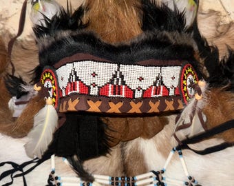 Puede incluir: Un tocado y peto nativo americano. El tocado presenta piel negra, detalles de cuentas en rojo, blanco y marrón, y plumas decorativas. El peto está adornado con cuentas y plumas, mostrando la artesanía tradicional y el patrimonio cultural.