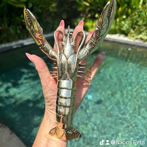 May include: A silver lobster sculpture with detailed claws and a textured body. The sculpture is held in a person's hand.
