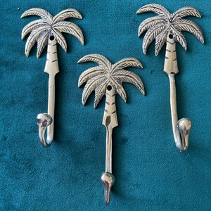 Puede incluir: Tres ganchos de palmera plateados. Los ganchos tienen forma de palmeras con un gancho curvo en la parte inferior. Los ganchos son una forma decorativa de colgar objetos en una pared.