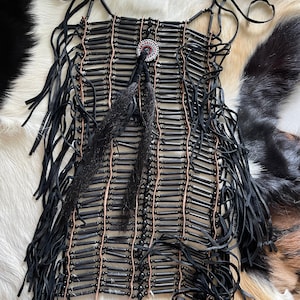Könnte beinhalten: Eine schwarze Perlenkette mit Fransen und einem kleinen runden Anhänger. Die Kette besteht aus schwarzen Perlen und Lederfransen.