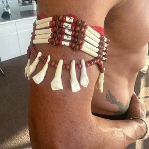 May include: A red and brown beaded bracelet with white bone accents. The bracelet is worn on a person's arm.
