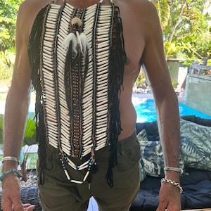 Peut inclure: Un plastron de style amérindien en perles blanches et noires avec une frange de plumes noires et de perles. Le plastron est porté par une personne au teint hâlé.
