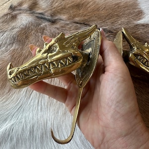 May include: A pair of gold dragon head hooks with a detailed design. The hooks are attached to a round metal plate.