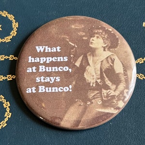 May include: A brown button with a vintage photo of a woman and the text "What happens at Bunco, stays at Bunco!"
