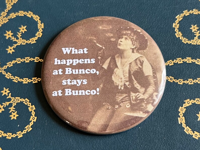 May include: A brown button with a vintage photo of a woman and the text "What happens at Bunco, stays at Bunco!"