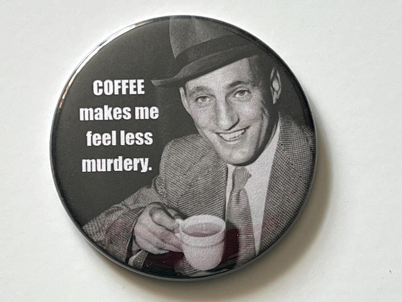 May include: A round, black and white button featuring a vintage image of a man in a suit and fedora holding a coffee cup. The text on the button reads, "COFFEE makes me feel less murdery."