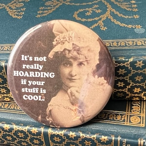 May include: A round button with a vintage photo of a woman with a large hat. The text on the button reads "It's not really HOARDING if your stuff is COOL."