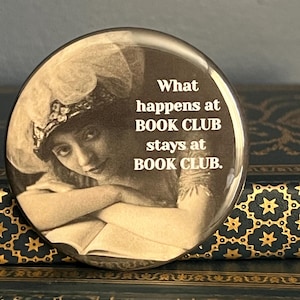May include: A round mirror with a vintage image of a woman reading a book. The mirror has the text "What happens at BOOK CLUB stays at BOOK CLUB." printed on it.