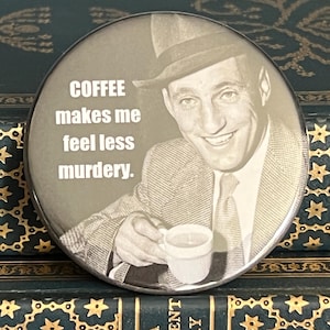 May include: A round button with a vintage image of a man in a suit holding a coffee cup. The text on the button reads "COFFEE makes me feel less murdery."